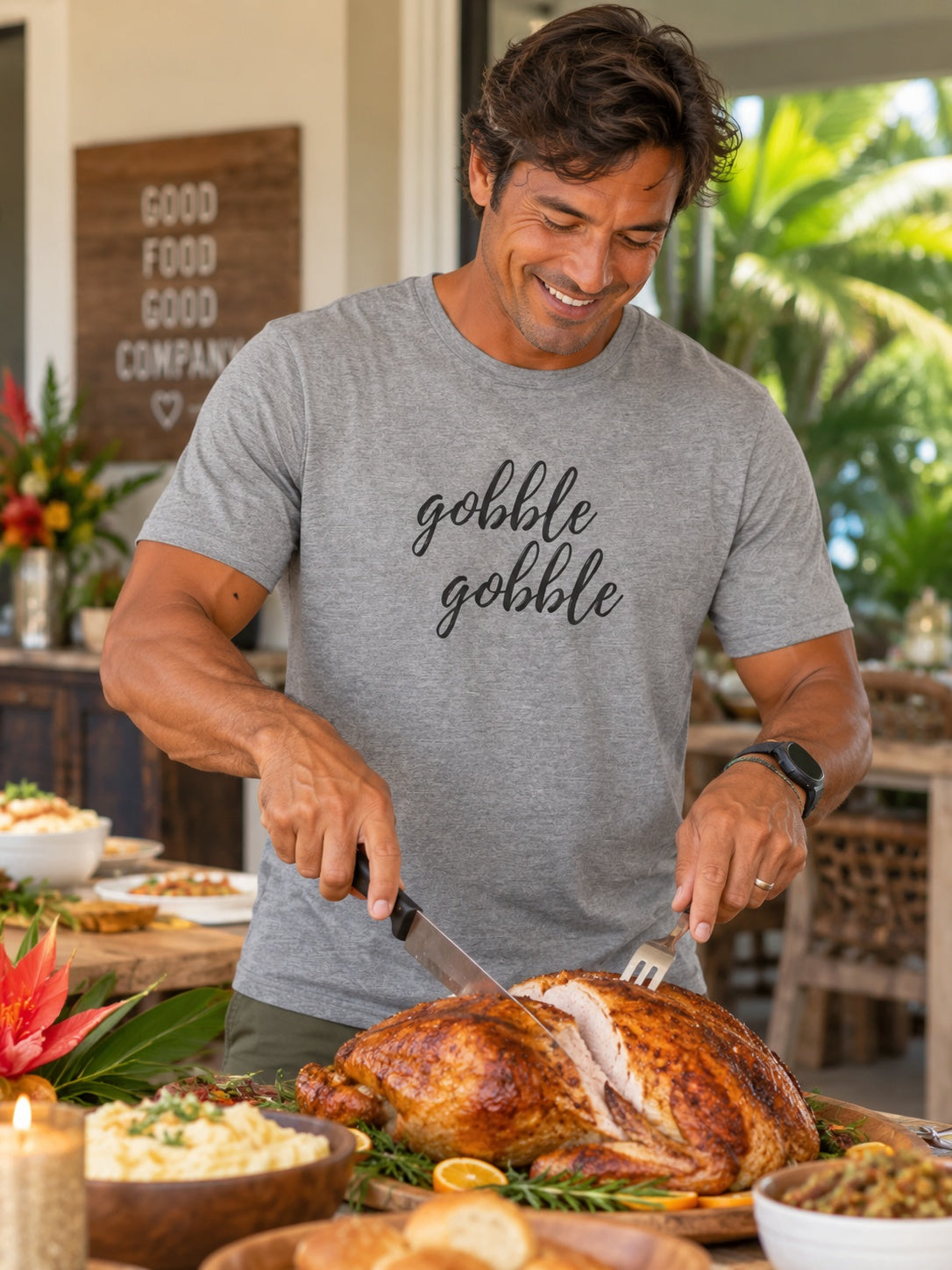 A smiling man carving a roasted turkey at a dining table, wearing a heather gray t-shirt with the phrase 'gobble gobble' printed in black script across the chest.