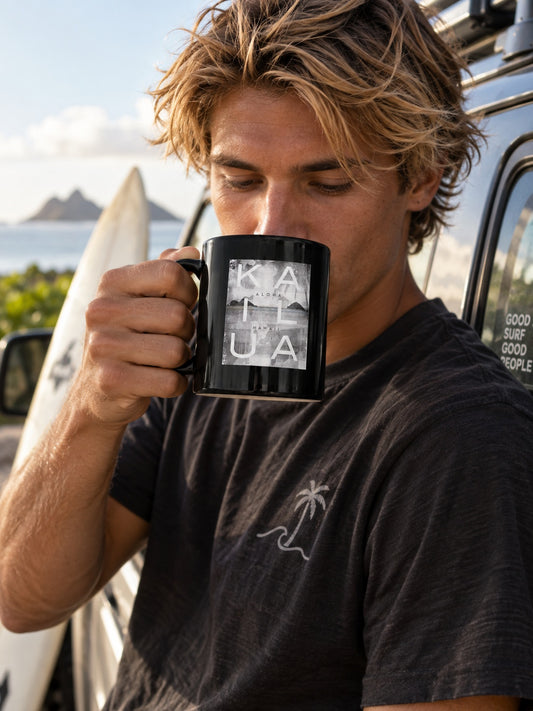 Surfer holding a Kailua Block black coffee mug while leaning against his car near the beach in Hawaiʻi.