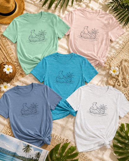Five women's short-sleeve graphic T-shirts in mint green, light pink, teal blue, dusty blue, and white, arranged in a flat lay with a tropical beach theme including palm leaves, a straw hat, flowers, and a woven mat.