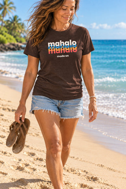 Woman wearing a brown retro Mahalo Mode graphic t-shirt while walking barefoot along a Hawaiʻi beach.