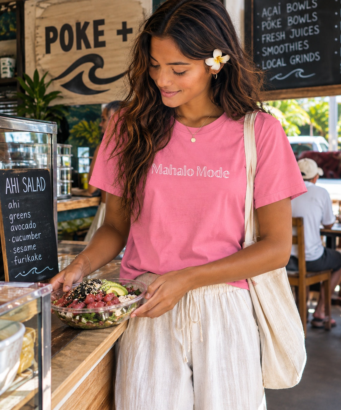 Woman wearing a pink Mahalo Mode t-shirt while getting an ahi salad at a casual local Hawaiʻi lunch spot.