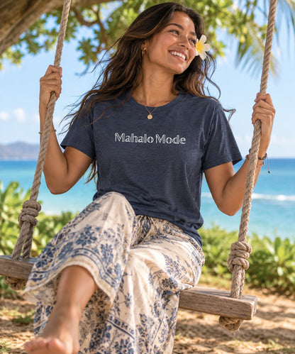 Woman wearing a heather navy Mahalo Mode t-shirt and boho pants while relaxing on an outdoor swing in Hawaiʻi.