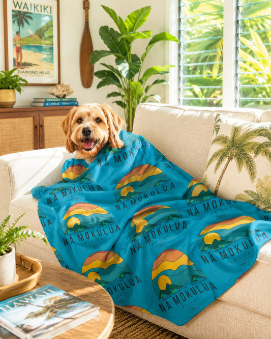 Nā Mokulua Kailua Hawaiʻi sherpa fleece blanket with colorful island print and plush cream backing draped over a dog on a natural couch in a tropical living room