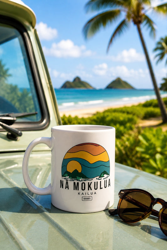 A white ceramic mug featuring a retro-style graphic of a sunset over mountains and waves, with the text 'NA MOKULUA KAILUA HAWAII' printed below sitting on top of the hood of a truck with sunglasses next to it and the beach in the background