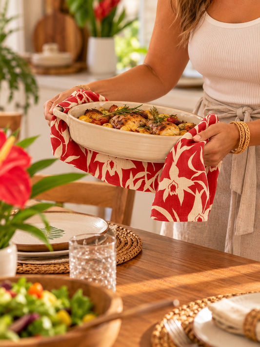Red Orchid Kitchen Towel — Woman carrying a warm baking dish with a red and cream tropical orchid kitchen towel.