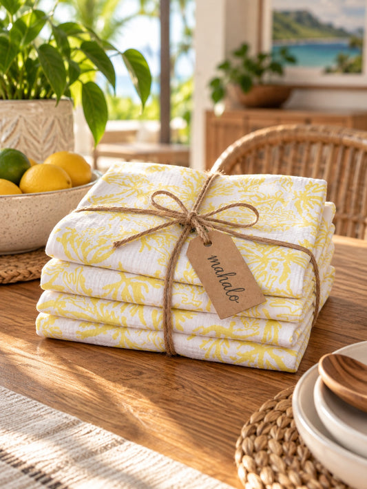 Stack of Coral Sunshine kitchen towels tied with jute string and a mahalo gift tag on a tropical kitchen table.
