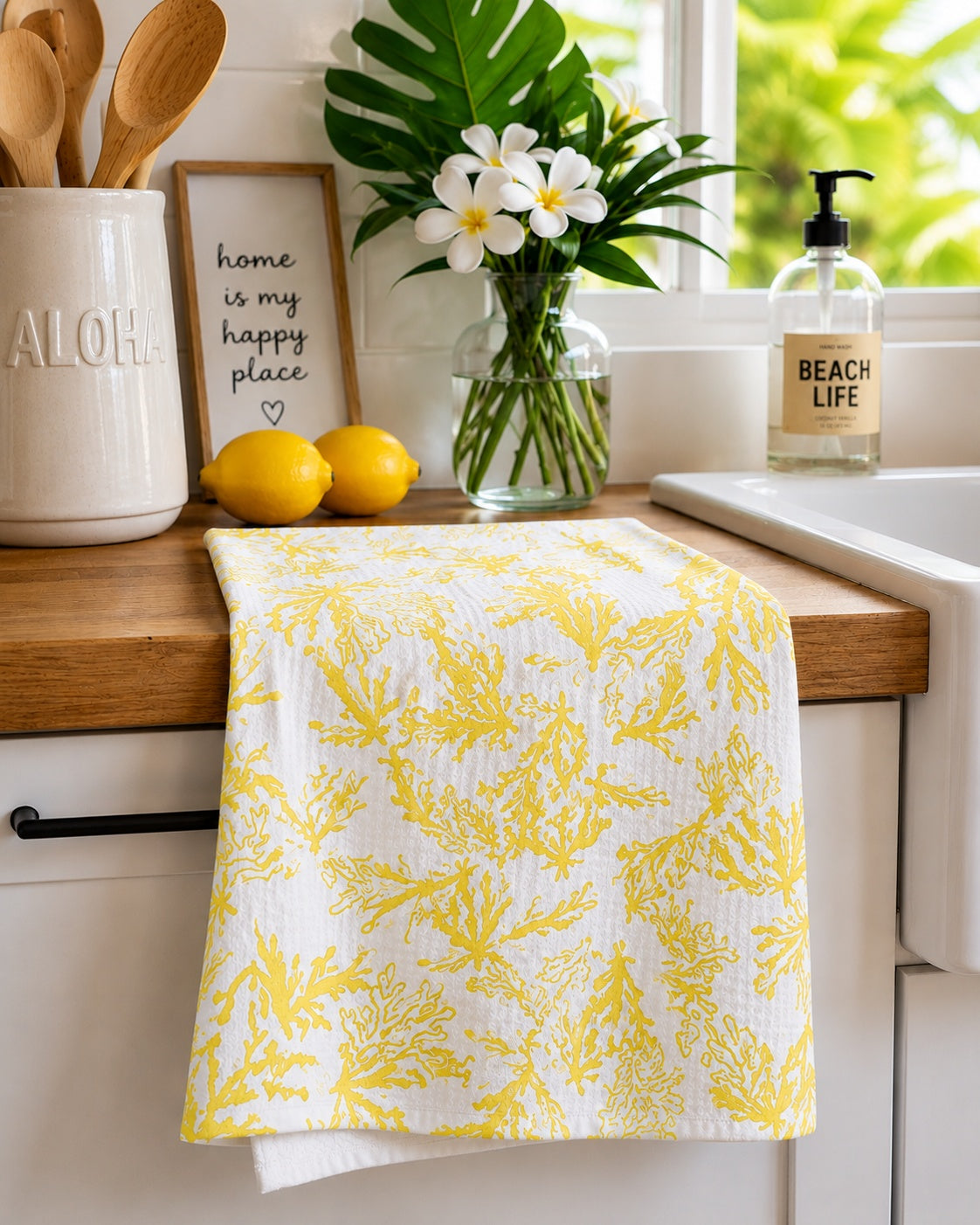 A white kitchen towel with a yellow coral pattern draped over a wooden countertop in a bright kitchen setting.