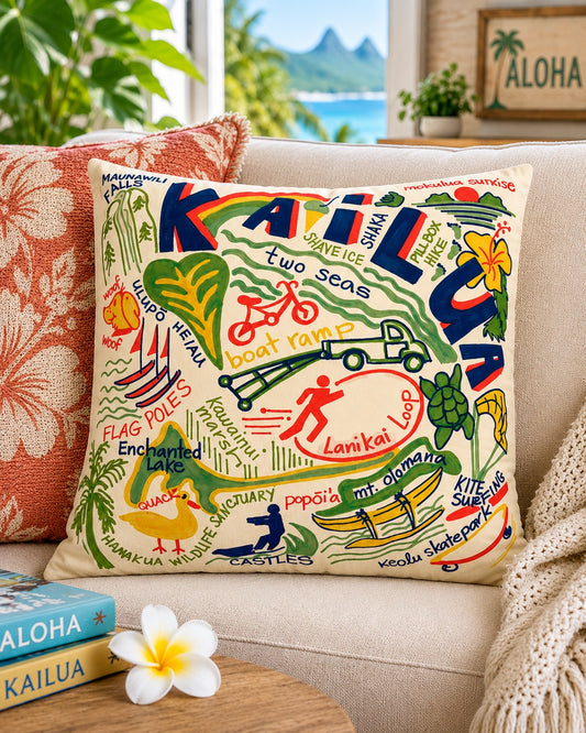 A square decorative throw pillow featuring a colorful Hawaiian-themed graphic print with the word 'Kailua' and local illustrations, styled on a beige sofa in a bright living room setting.
