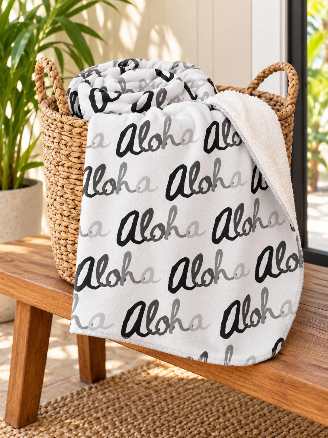 Aloha Grayscale sherpa fleece blanket draped from a woven basket on a wooden bench in a bright tropical entryway.