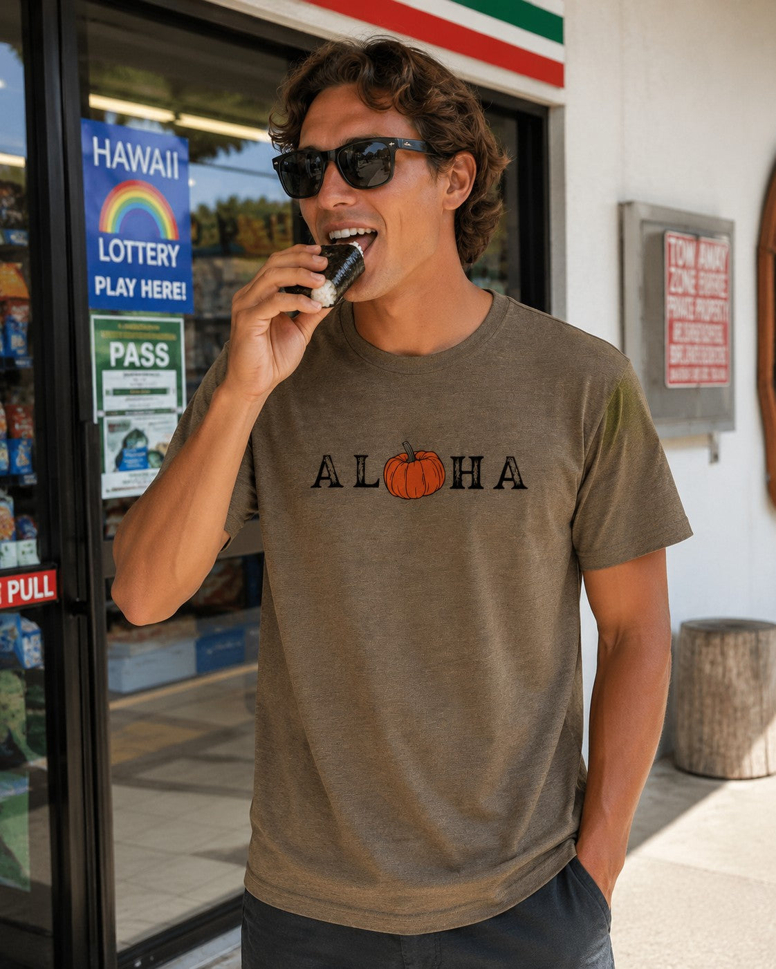 A man wearing an olive graphic t-shirt with 'ALOHA' and a pumpkin graphic printed on the chest, standing outside a convenience store.