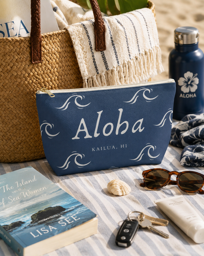 Aloha Wave T-Bottom Zip Pouch displayed with beach essentials on a striped towel beside a woven tote at the beach.