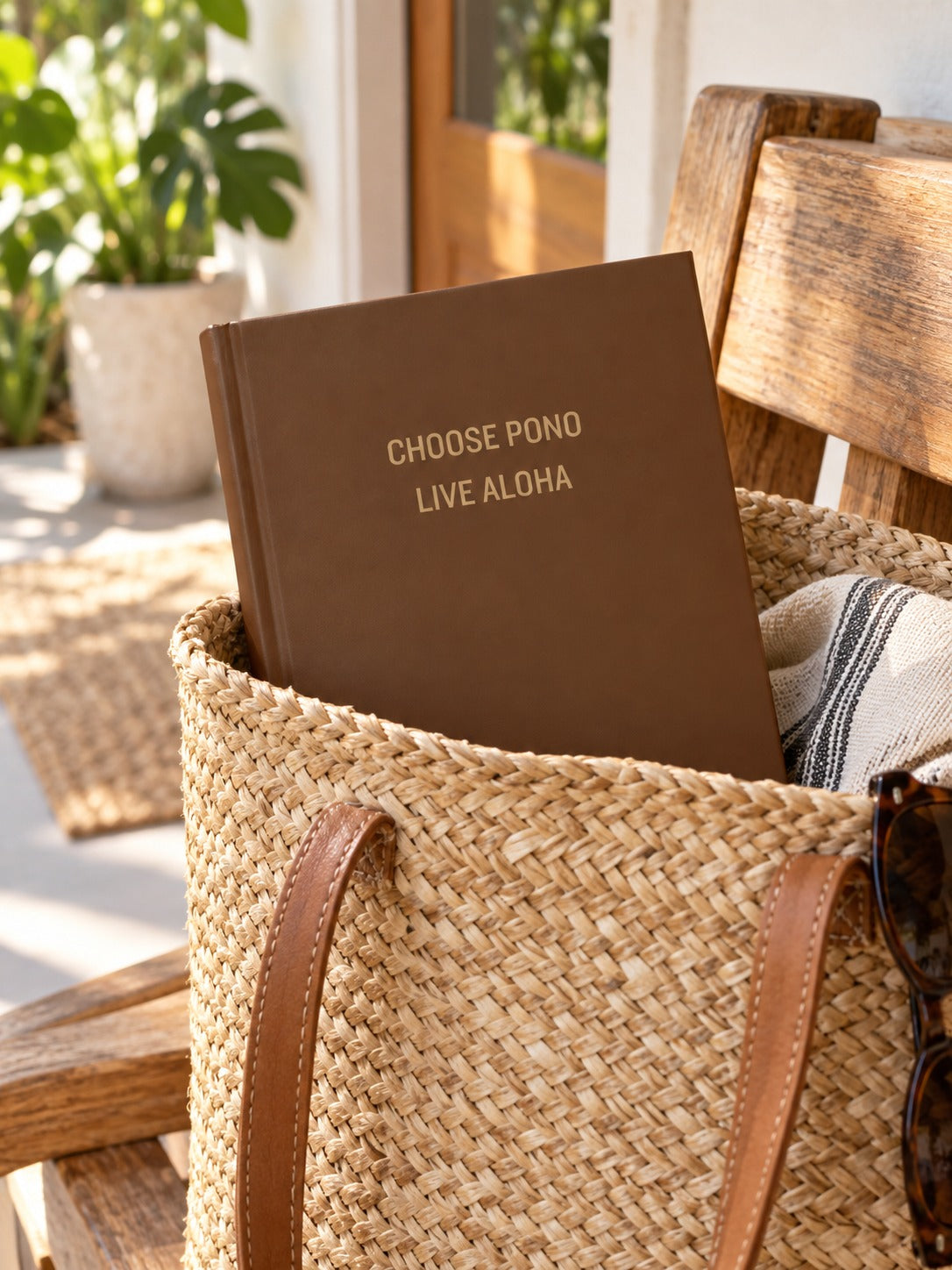 Brown Choose Pono Live Aloha hardcover journal tucked inside a woven straw tote in a bright tropical home.