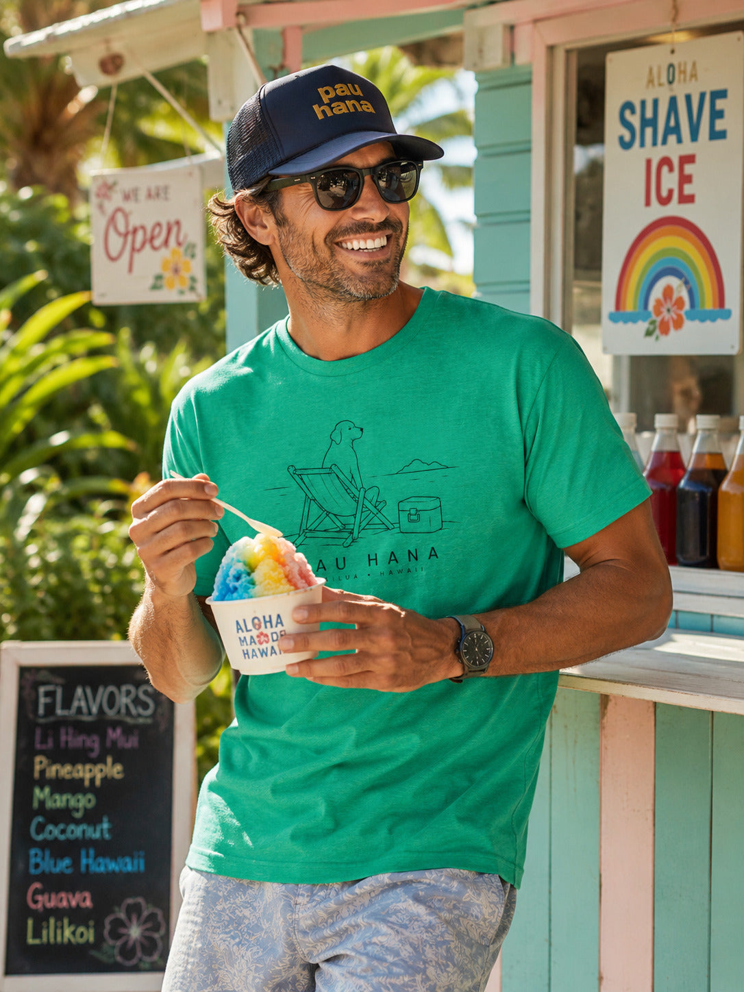 Man eating shave ice wearing a pau hana hat and Green t-shirt with a graphic design and 'PAU HANA' 