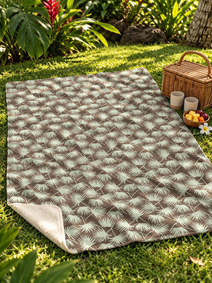 Fan Palm Mocha Mint sherpa fleece blanket spread on a tropical garden lawn with a picnic basket and fruit.