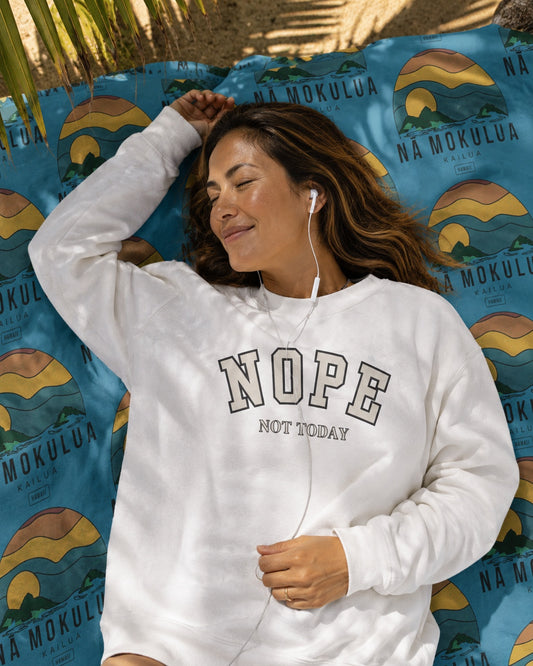 A woman lies on a blue patterned blanket outdoors, wearing a white sweatshirt with the words 'NOPE NOT TODAY' printed across the front.
