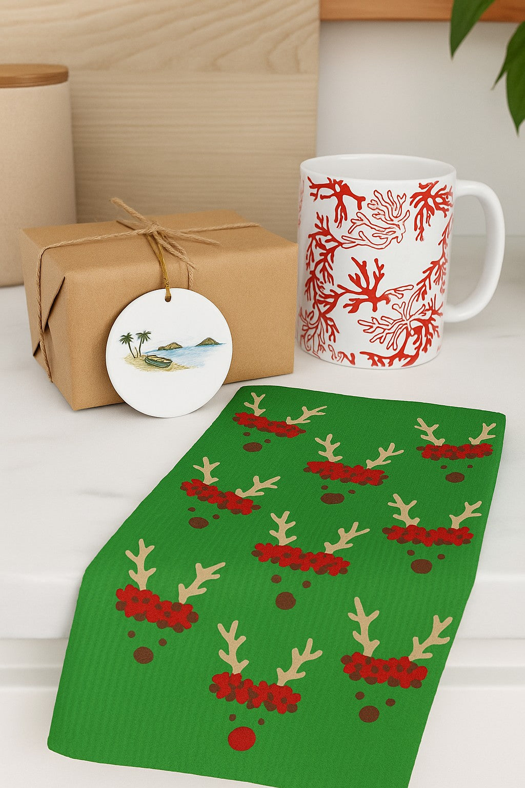 Green Reindeer and Rudolph holiday kitchen towel styled with a tropical mug and wrapped gift